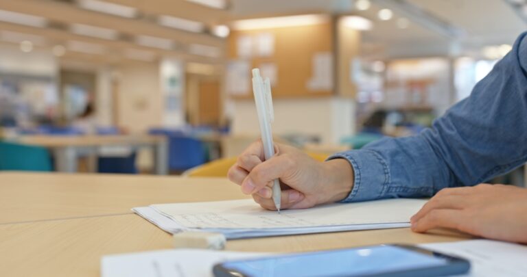 Woman work on the essay with using mobile phone in the library